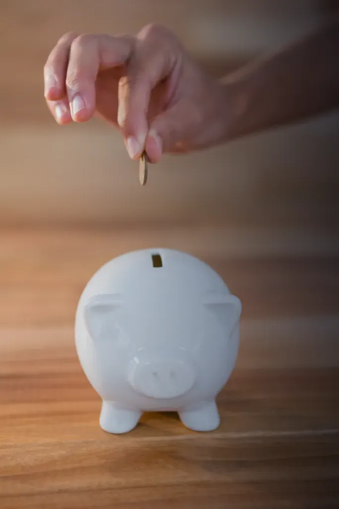 Mano deposita una moneda en una alcancía blanca.