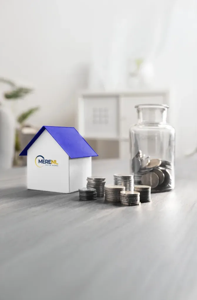 Casa de cartón con el logo de MERENL junto a pilas de monedas y un frasco con monedas.